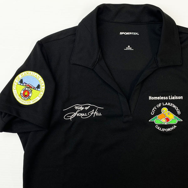 A black short-sleeve polo shirt with embroidered patches and text on the chest and sleeve. The collar shows the brand name 'SPORTFEX' inside.