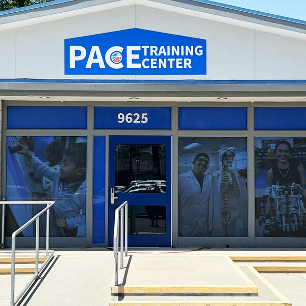 PACE Training Center storefront with a large blue and white sign above the entrance, glass windows with fitness and medical-themed posters, and a concrete walkway with metal railings.