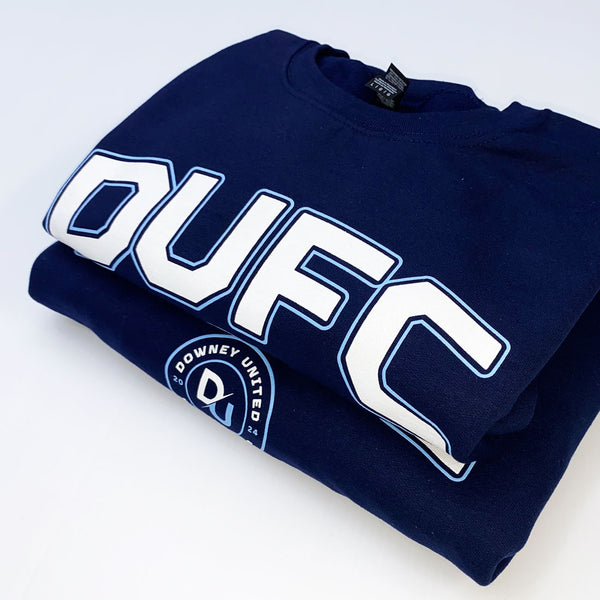 A folded navy blue sweatshirt featuring a large white 'DUFC' graphic with a light blue outline across the chest, and a circular 'Downey United FC' crest printed near the lower left front.